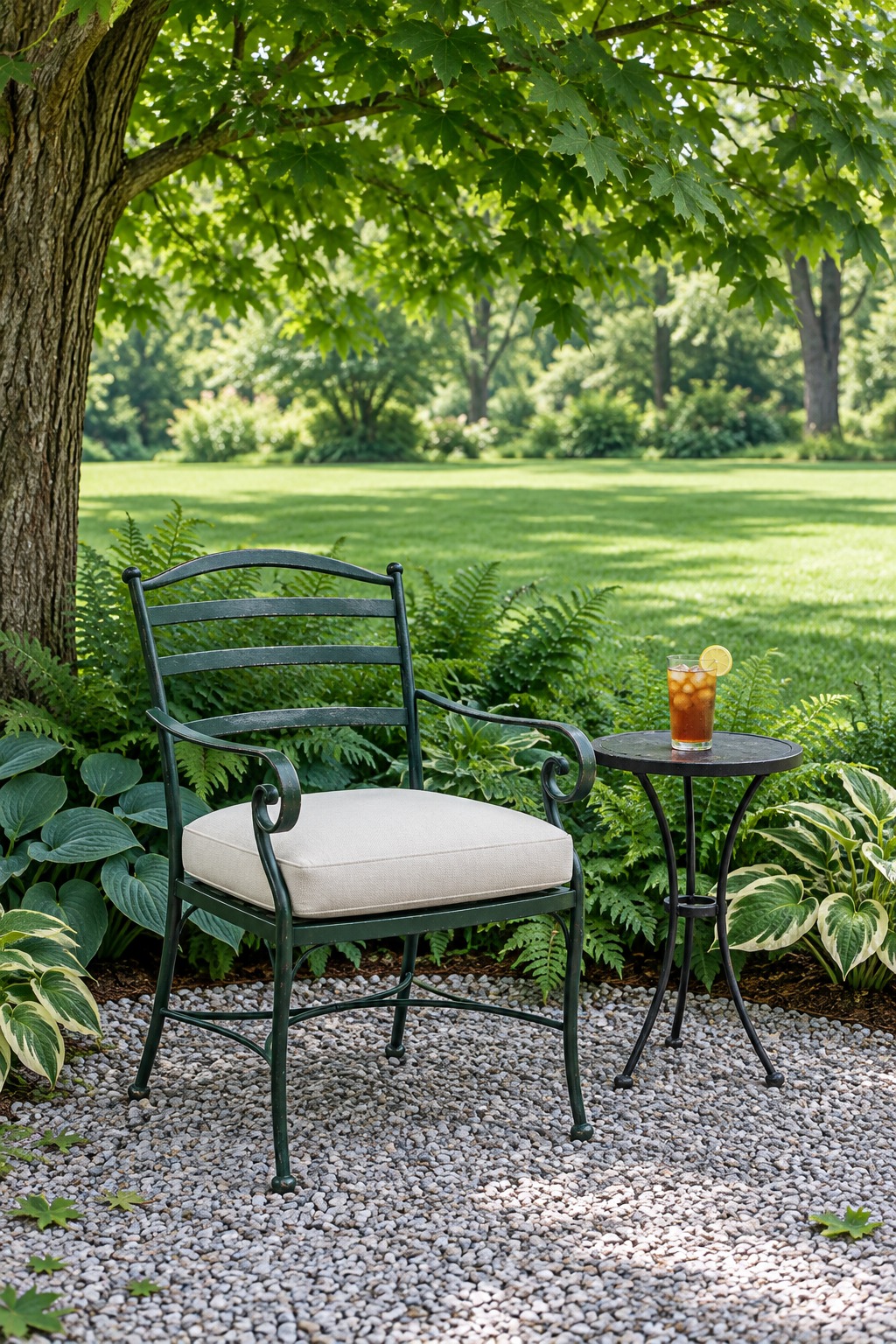 Green metal armchair with a cream cushion in the dappled shade of a maple tree beside hostas and ferns