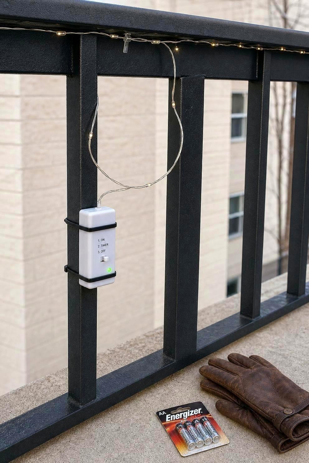 Fairy-light battery pack secured at hand height inside a metal balcony rail