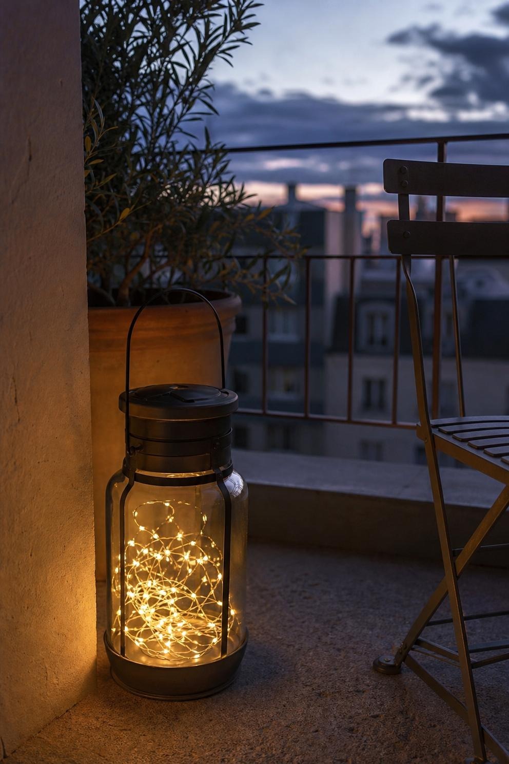 Short warm fairy-light strand coiled inside a weather-safe lantern beside a small balcony chair