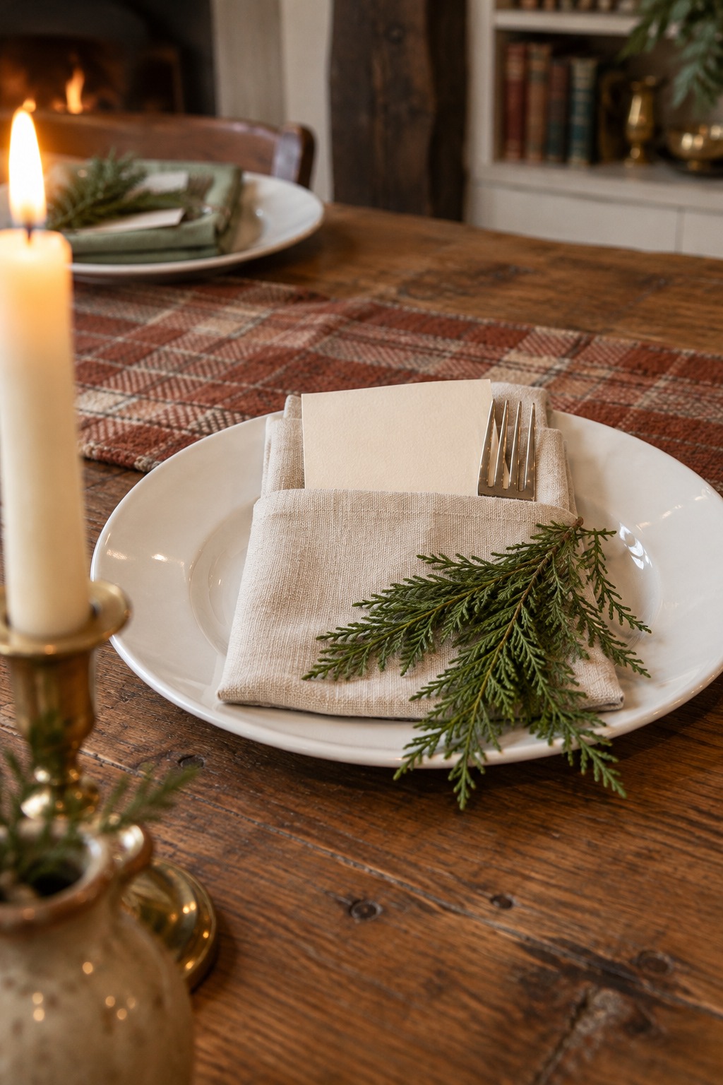 Close view of a white plate with a linen napkin folded into a pocket holding a fork and a small cream menu card, with a cedar sprig on top