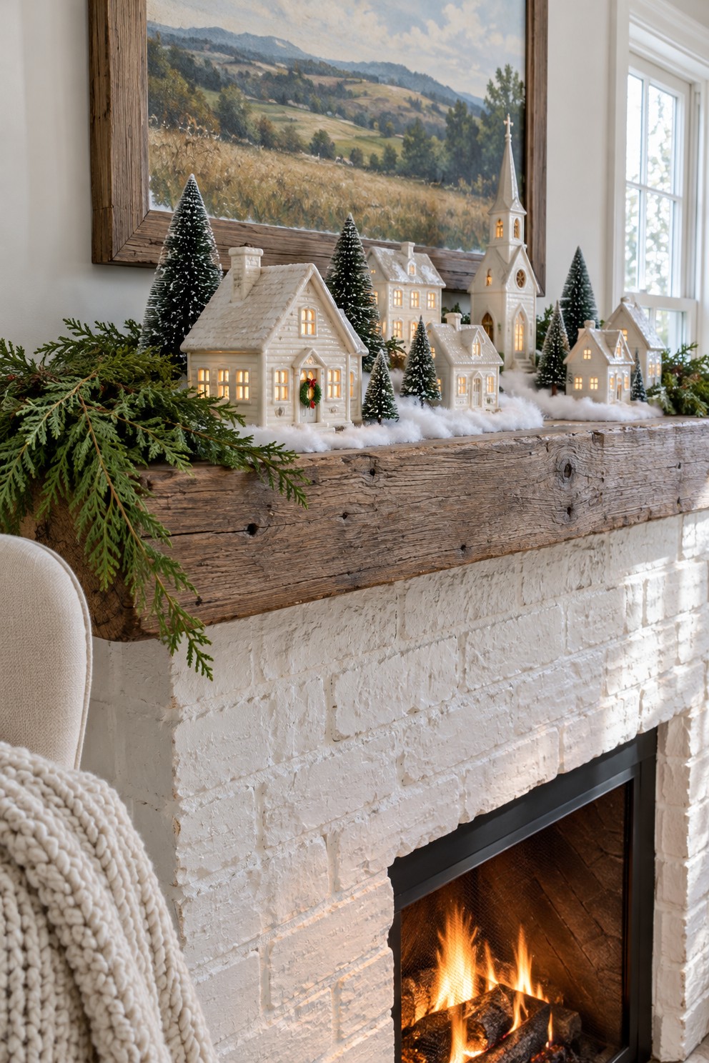 Small white Christmas village with a church and bottle-brush trees along a rustic wood fireplace mantel