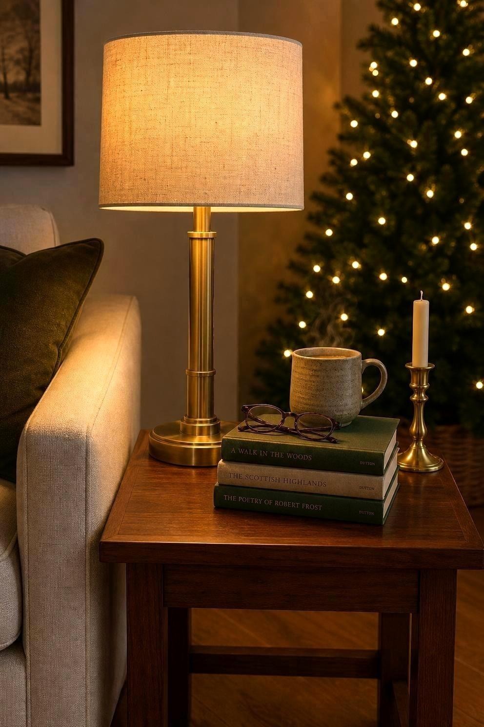 Lit brass table lamp beside books and a mug with a Christmas tree behind it