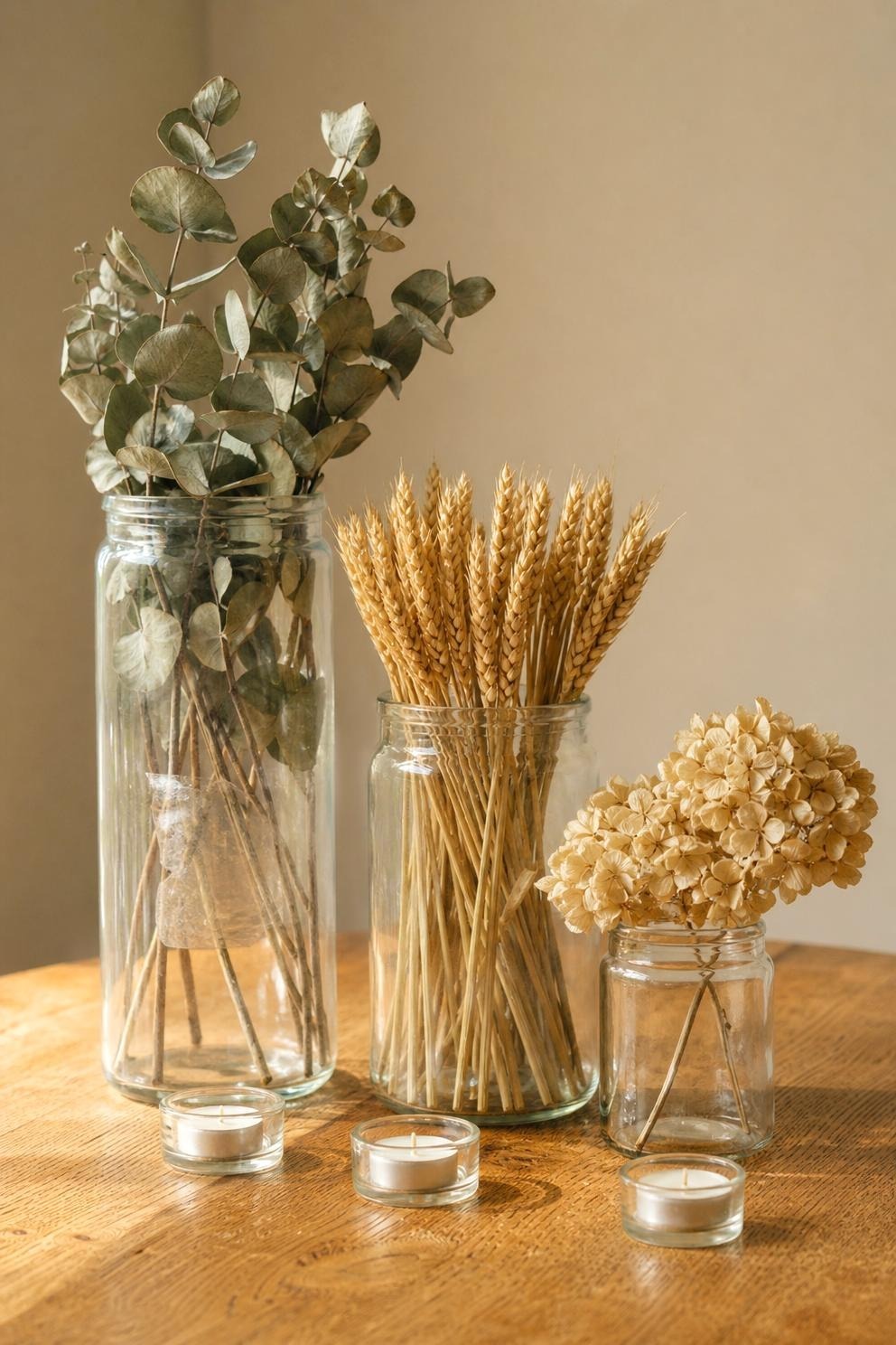 Glass jars holding eucalyptus, wheat and dried hydrangea on a wooden table