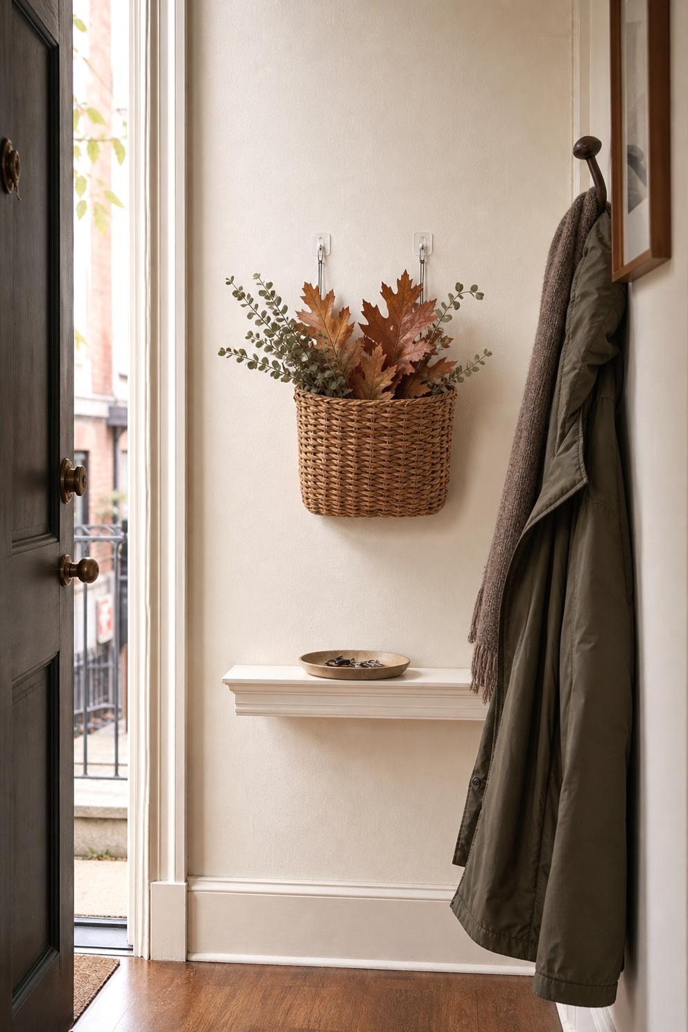 Oval wood mirror above a small entry table with clipped rust leaves and an amber bud vase