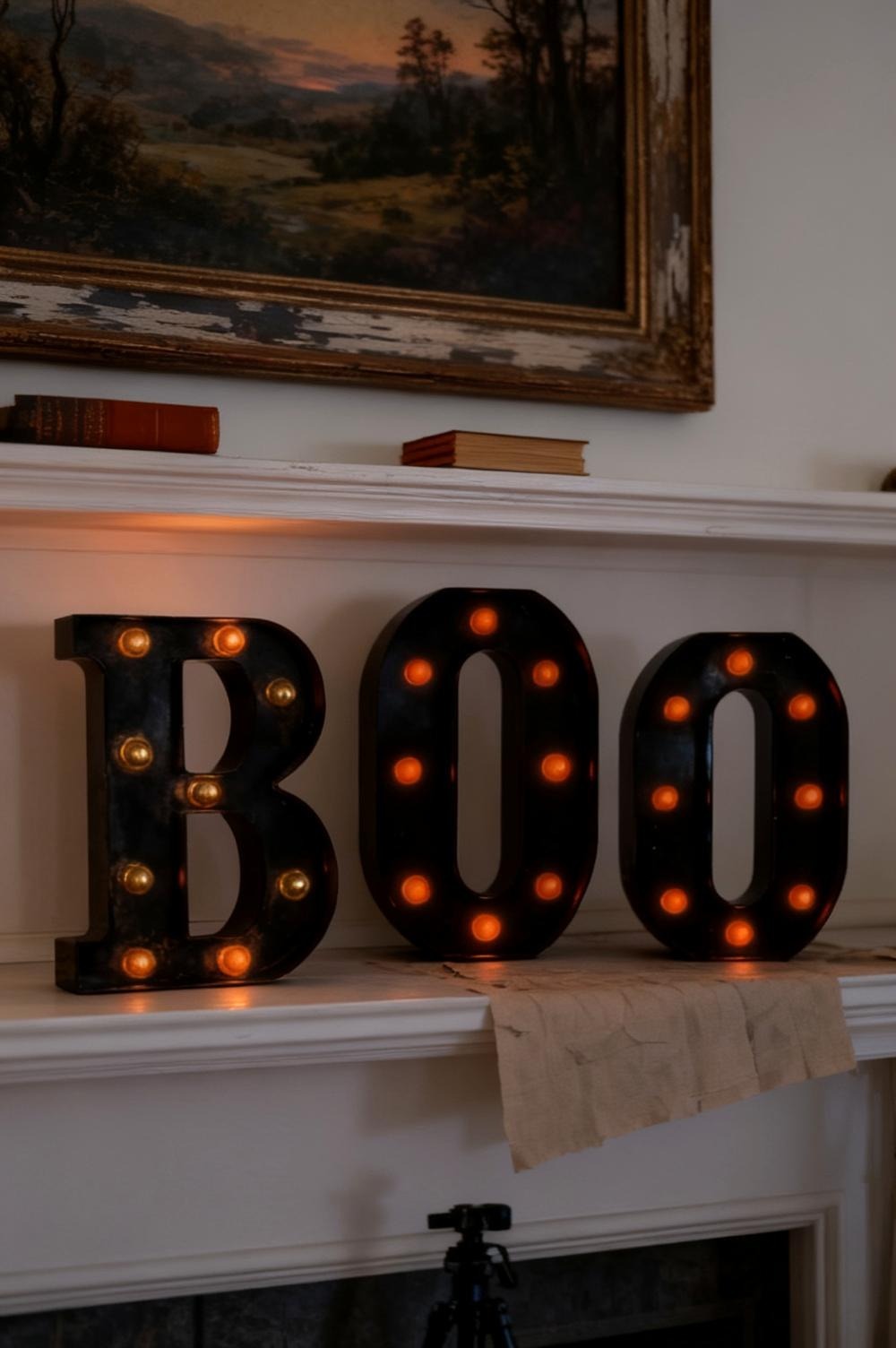 Black BOO marquee letters glowing on a cream fireplace mantel