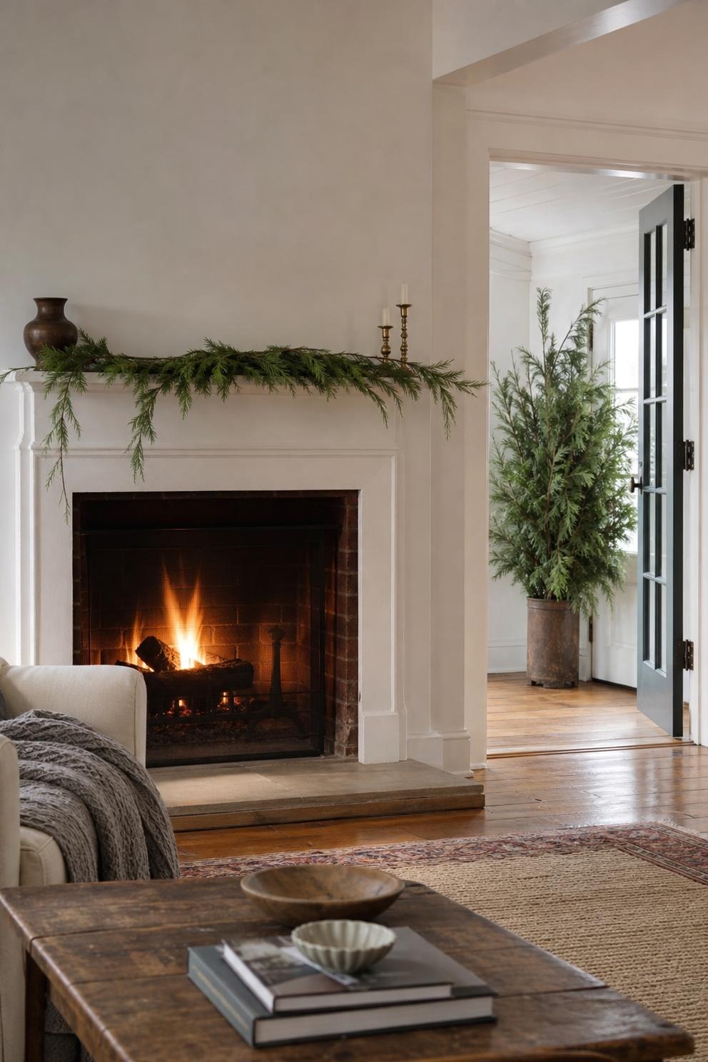 Simple faux garland on a working fireplace mantel with fresh cedar branches displayed in a cool doorway across the room
