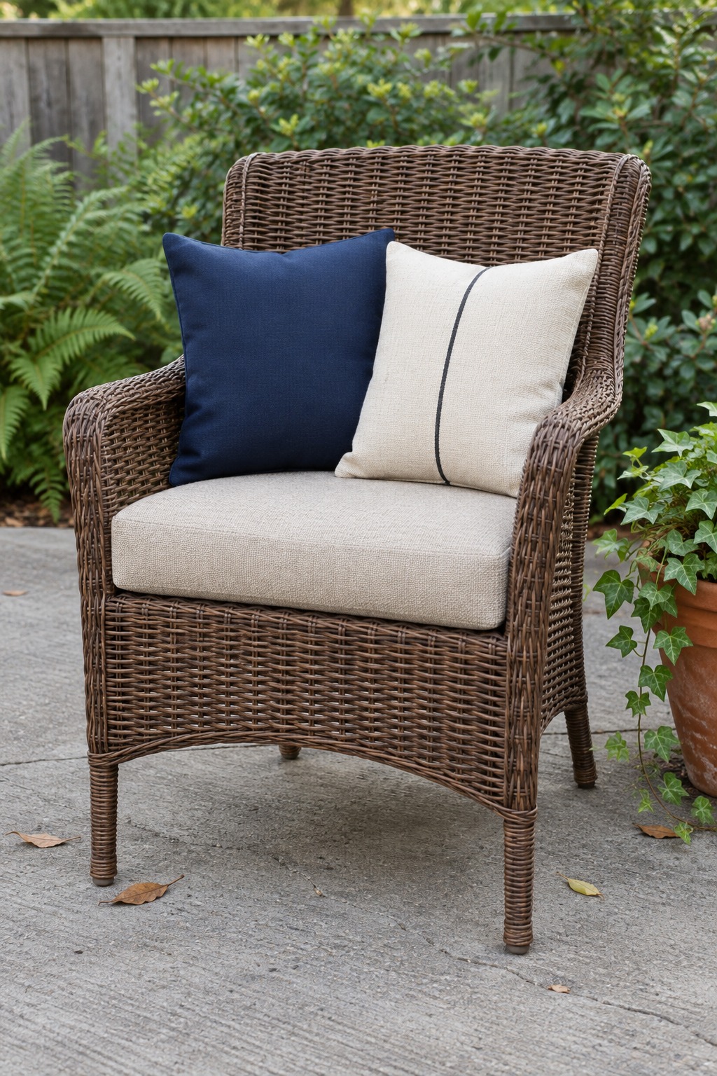 Navy pillow and cream pillow with a thin black stripe on a brown wicker patio chair with a beige seat cushion