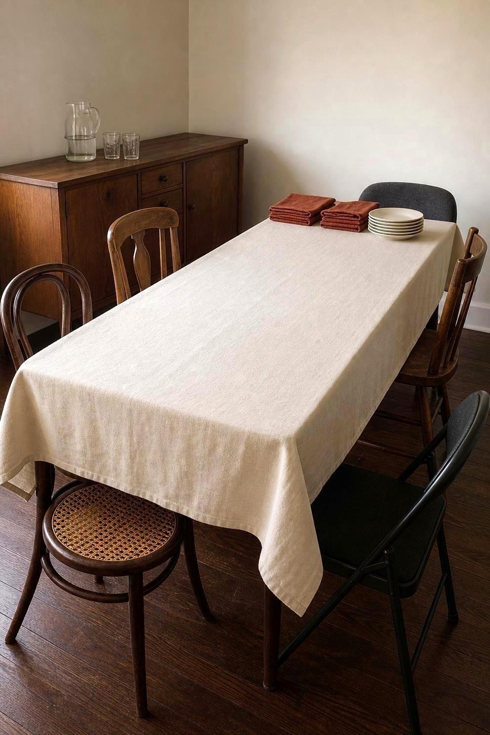 A six foot folding table butted end to end against a smaller wooden dining table, both covered by one long cream tablecloth so they read as a single surface