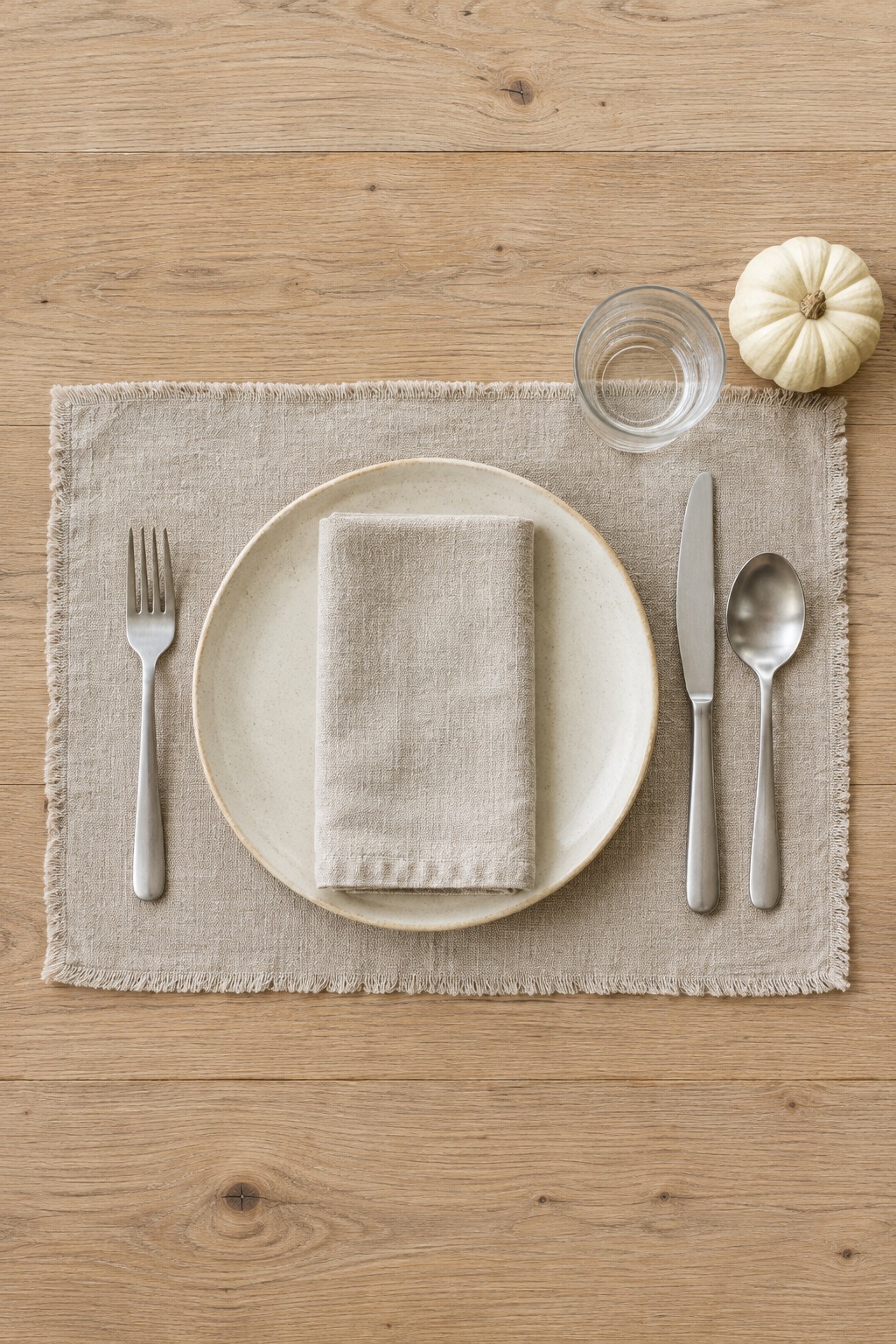 One place setting from above: cream plate with an oatmeal napkin, fork on the left, knife and spoon on the right, glass above the knife